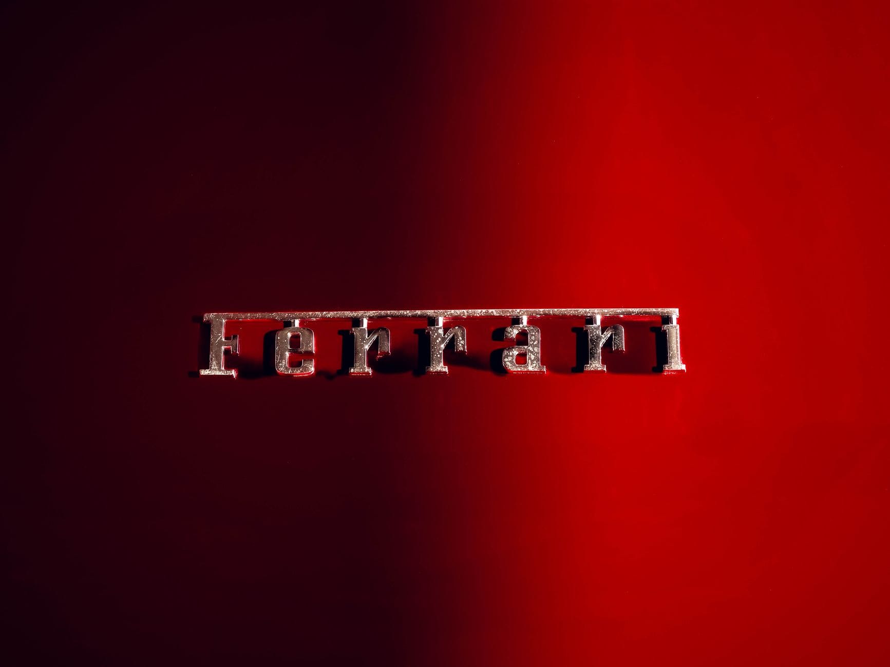 Detailed shot of a Ferrari emblem on a sleek red background, showcasing luxury automotive design.