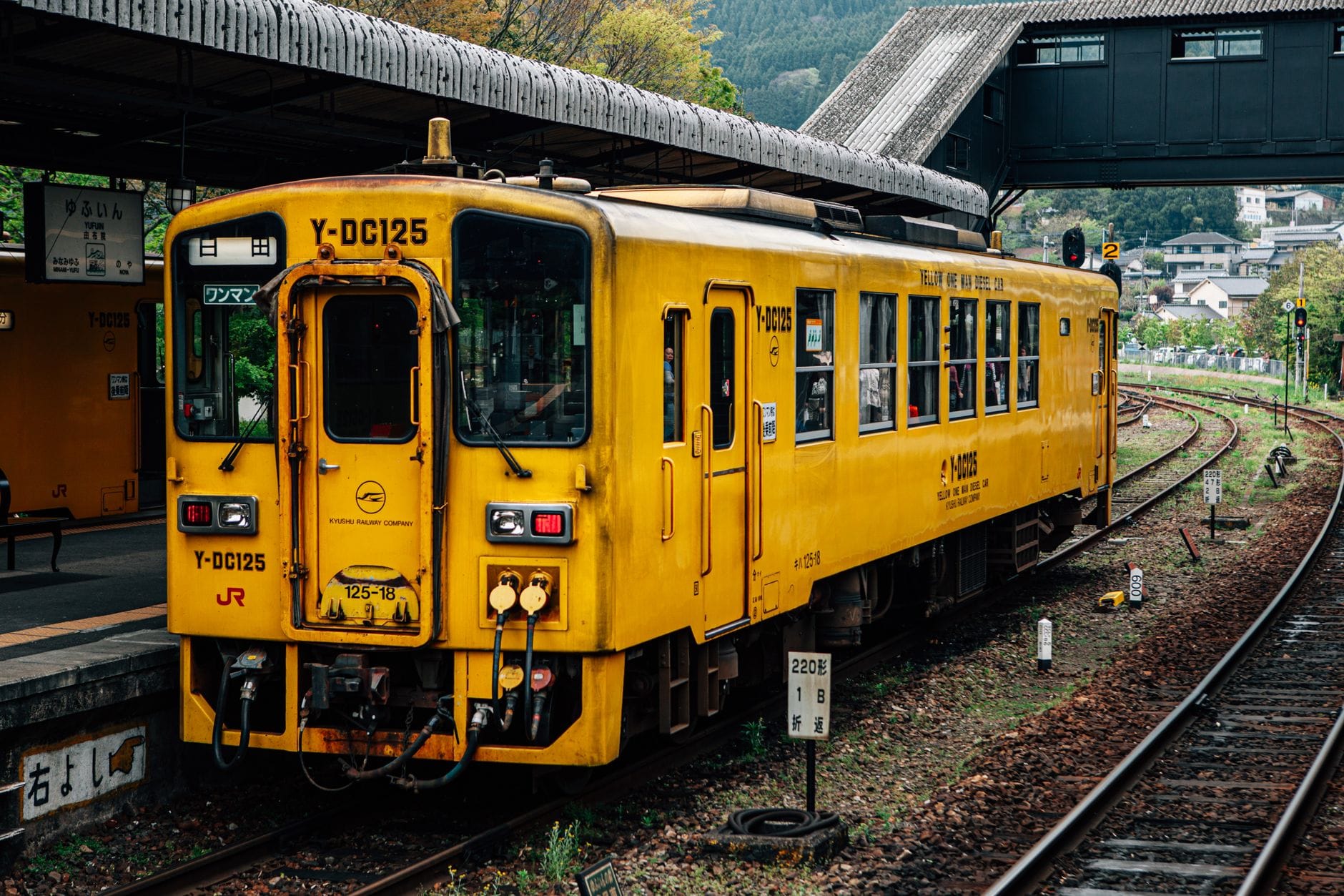 Bright aged train car on narrow railroad near roofed platform behind houses in suburb